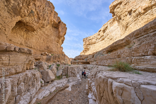 Tourists in a hiking trail in dry wadi Upper Darga in the nature reserve Matzok HaEtekim, Judaean Desert. A narrow canyon with high walls. photo