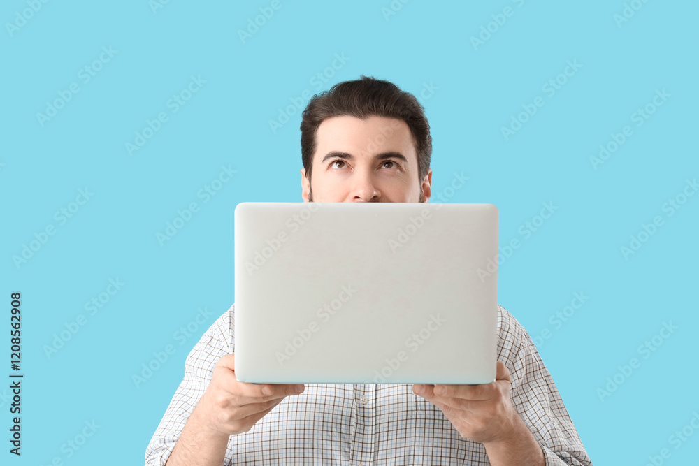 Handsome man with laptop looking upwards on blue background