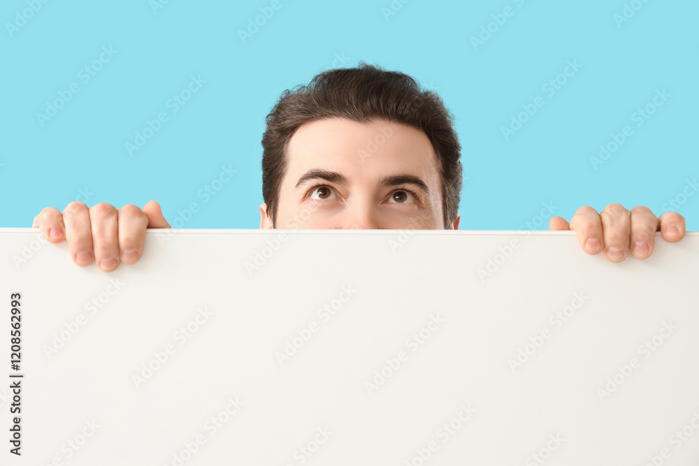 Handsome man with blank poster looking upwards on blue background, closeup Handsome man with blank poster looking upwards on blue background, closeup
