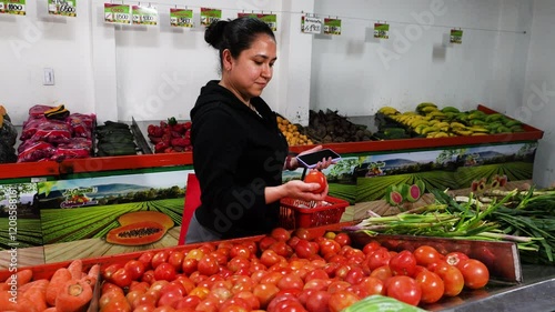A female domestic worker is buying some fruits and vegetables in a store. It's in front of the tomatoes