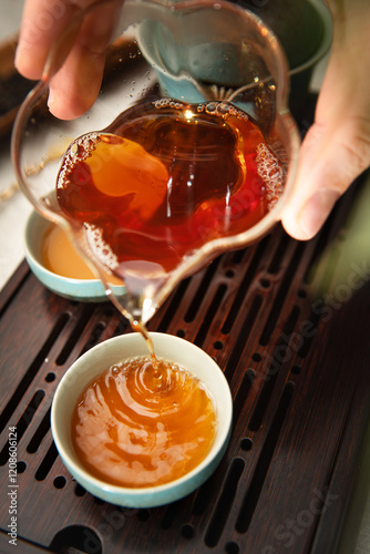 Female hands pouring tea from clear glass pitcher teaware into tea cups, creating serene tea ritual. Soft light, wooden tea tray evoke calming mindful Chenese ceremony atmosphere. photo