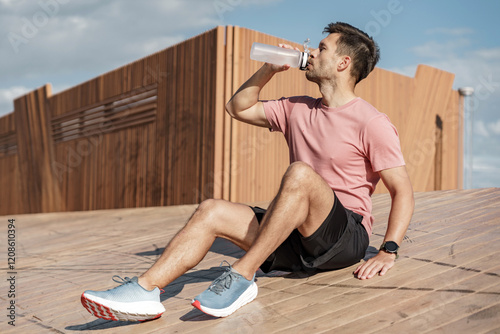 Man in athletic wear relaxing and hydrating on a wooden structure outdoors during daylight photo