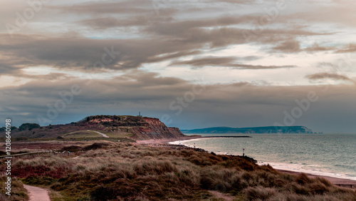 A scenic view of Southbourne beach with cliffs, dunes, and coastal paths under a cloudy sky. The tranquil sea and distant horizon create a peaceful and picturesque coastal landscape. photo