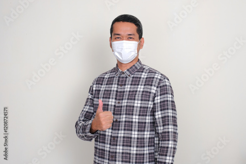 Adult Asian man wearing medical face mask give thumbs up photo