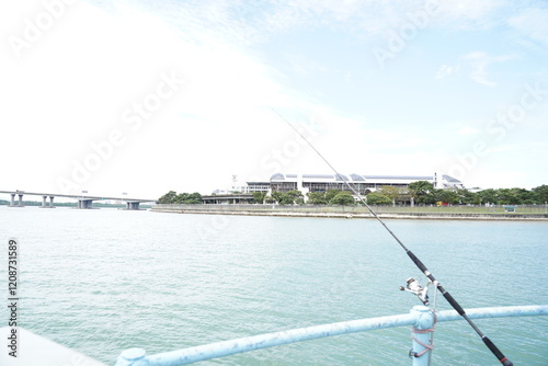 A fishing rod in action captures the essence of leisure fishing, set against a backdrop of nearby facilities and a bridge, blending recreational activity with urban infrastructure.