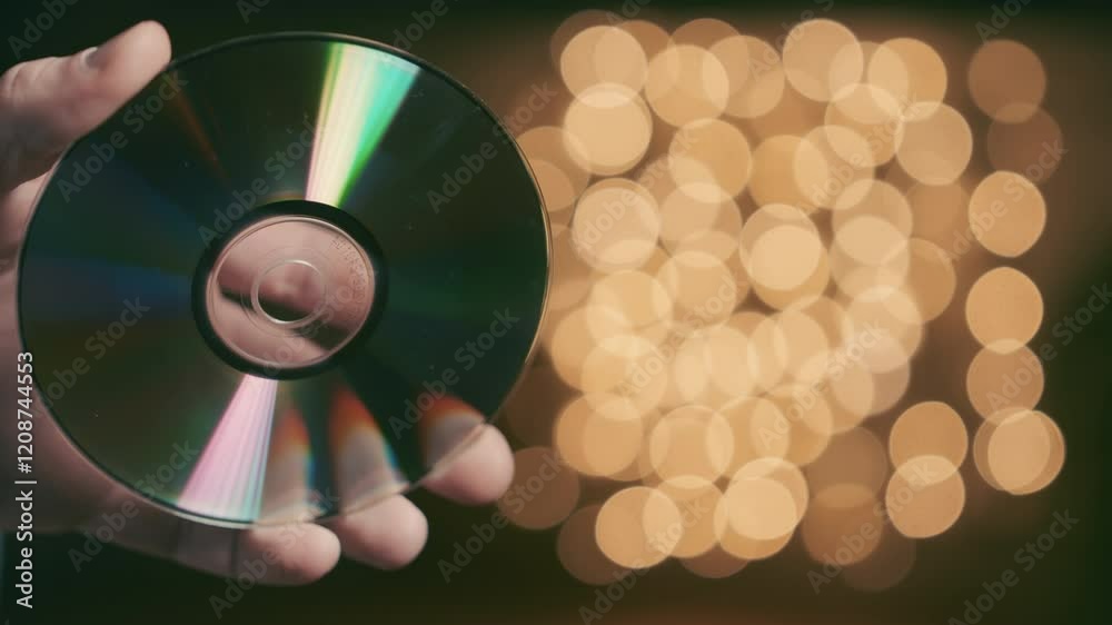 CD Disc Rotating in Hand with Rainbow Reflection, Compact Disc with Light Effects and Golden Bokeh Background, Digital Media Close Up