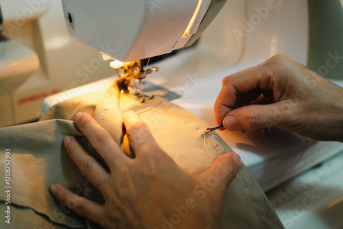 Woman hands using seam ripper tool to unstitch the thread while sewing light brown fabric with sewing machine