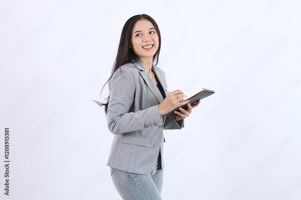 smiling woman in a gray blazer smiling and writing on book with a pen.. Business asian woman smiling woman in a gray blazer smiling and writing on book with a pen.. Business asian woman