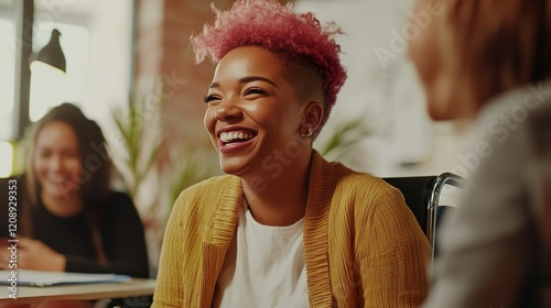 Inclusive image of a happy mixed race lesbian employee sitting in a wheelchair laughing with colleagues in a team meeting. Disabled black working woman with pink hair. Inclusion diversity workplace