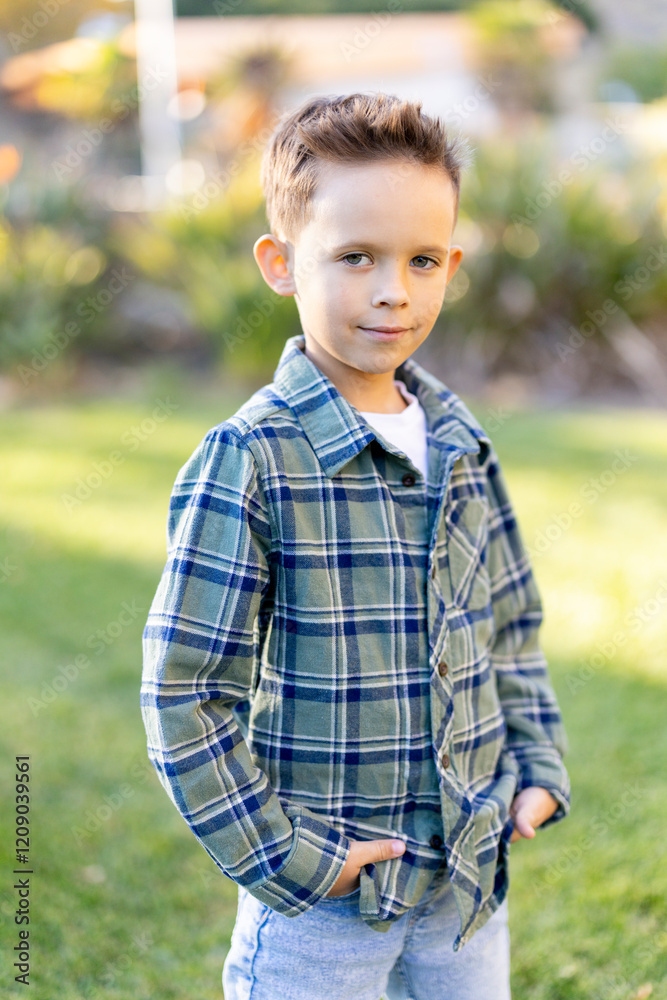 A charming, lively young boy dressed in a stylish plaid shirt poses confidently in a bright grassy area, showcasing his playful innocence against a vibrant outdoor setting filled with color and light A charming, lively young boy dressed in a stylish plaid shirt poses confidently in a bright grassy area, showcasing his playful innocence against a vibrant outdoor setting filled with color and light