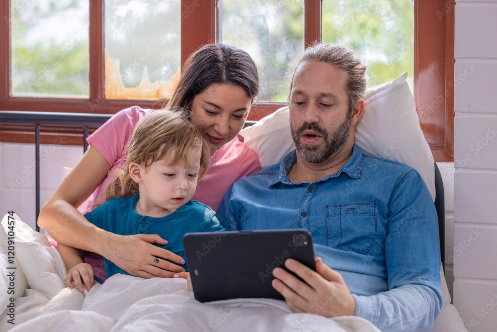 © SpaceOak - Family enjoying a cozy morning together while watching a tablet in bed