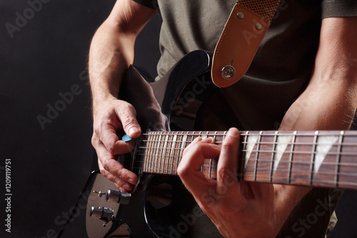 Hands of rock guitarist playing the black guitar on dark stage.