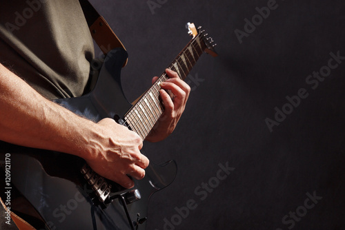 Posing hands of rock guitarist playing the black guitar on dark stage.