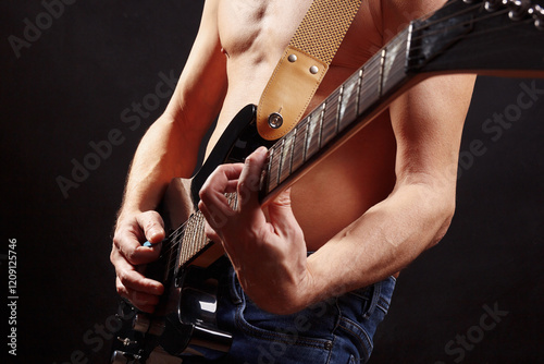 Artist playing chord on guitar on dark stage.
