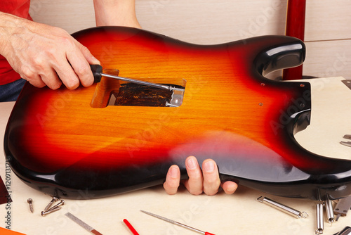 Guitar technician screws the holder of tremolo springs in guitar body.