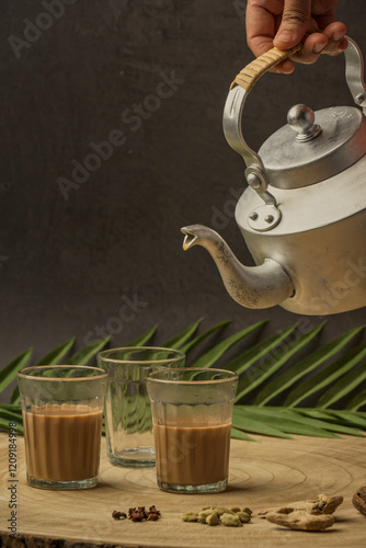 Indian masala chai tea. Masala chai spiced tea with milk and spices or karak chai or cutting chai. Tea being poured into glasses from a kettle and spices on isolated background.