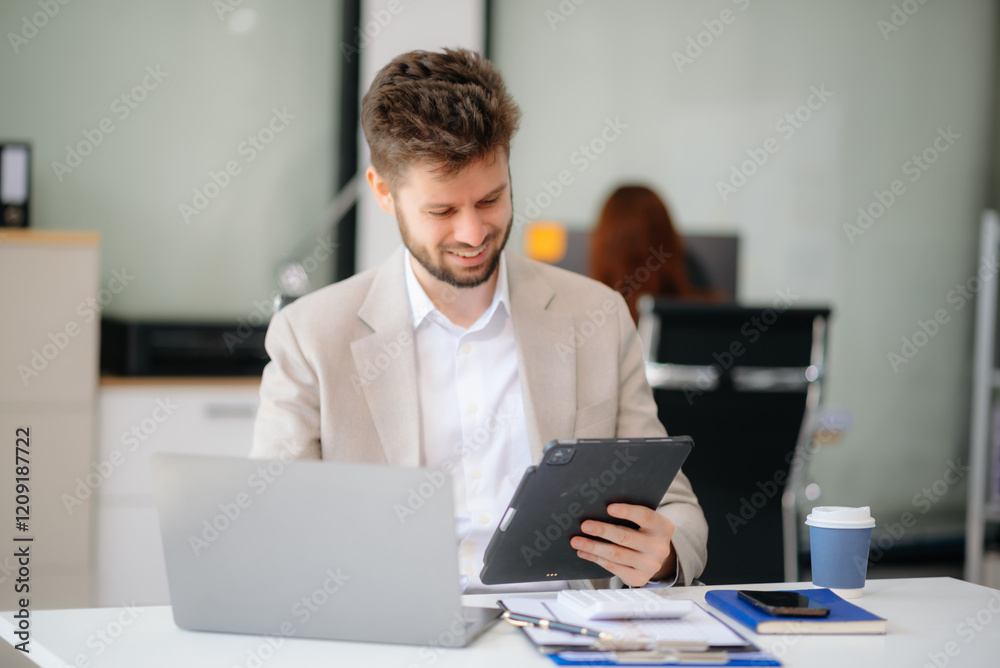 Confident businessman working on finance analysis with a tablet and laptop at office desk. Confident businessman working on finance analysis with a tablet and laptop at office desk.