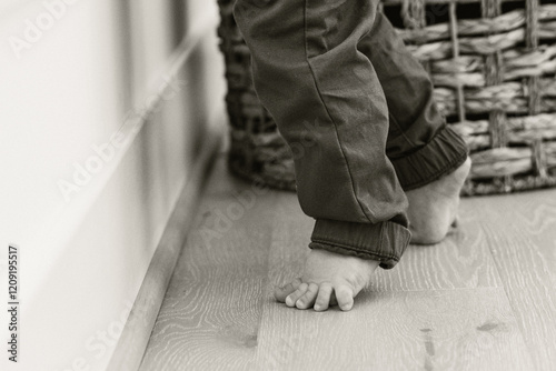 Barefoot toddler standing on wooden floor near a wicker basket photo