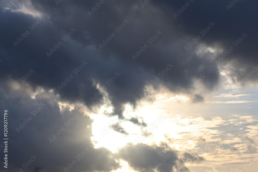 Dense gray clouds and bright last sun lays with white clouds around