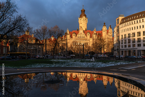 Picture taken at sunset of the new town hall in Leipzig. Picture taken in winter with a reflection of the building in the foreground. Brightly lit town hall against a dramatic dark sky.