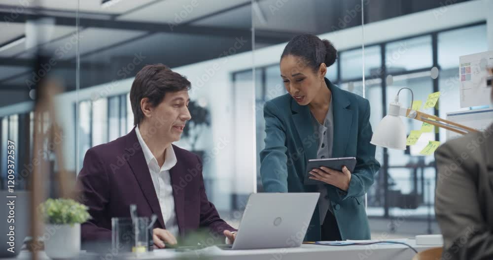 Young Female Manager Talking with Experienced Male Colleague while Using Laptop and Tablet Computers in Office. Colleagues Discuss Business, Financial and Marketing Projects. Specialists Work Together