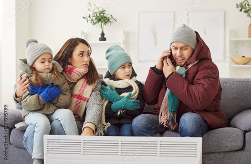 Annoyed family in cold winter room, dissatisfied parents, children near heater warming air, flat renter in upper wear, tenants calling apartment management company to complain on bad low temperature photo