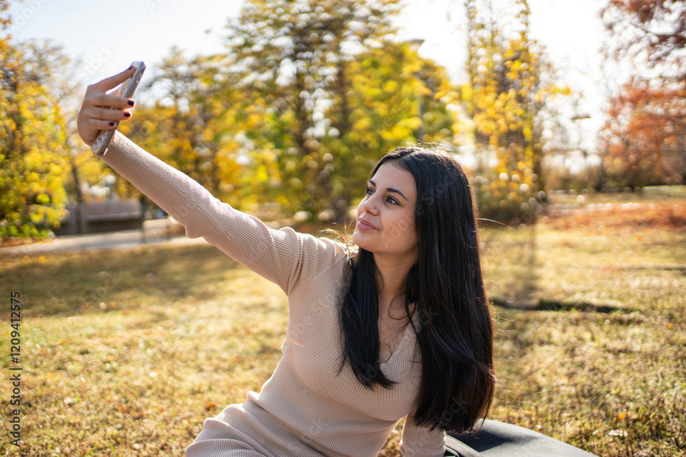 Naklejka premium Young woman taking selfie in autumn park using smartphone