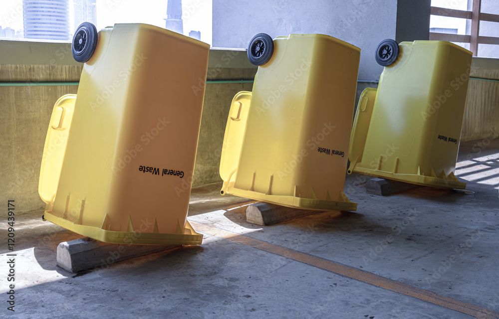 Perspective view of Yellow large plastic rubbish bins and turn upside down to dry near concrete wall on parking lot of condominium building. After cleaning big plastic yellow garbages container.