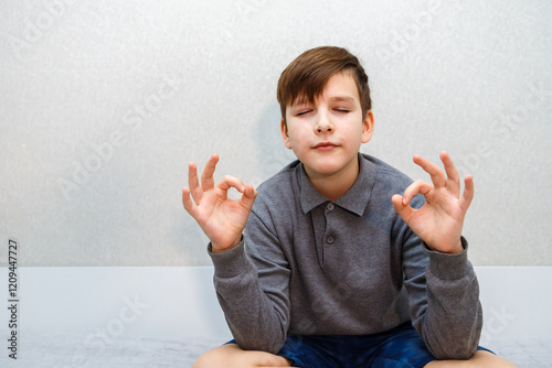 ten year old boy meditating in lotus position. in grey sweater against grey wall photo