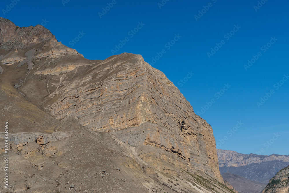 Fototapeta premium Kabardino-Balkaria. El-Tyubu. Rocky mountains with trees growing on their slopes glow in morning sun. Close-up. Chegem Gorge. Unique rocky ridge with steep cliffs against blue autumn sky.