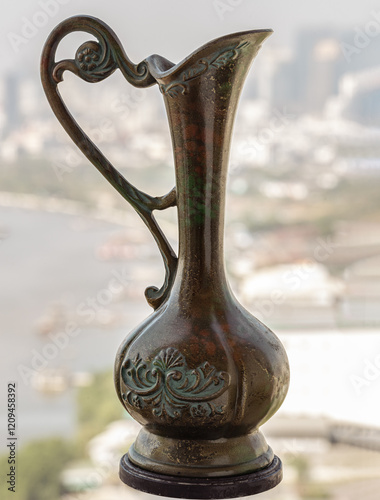 Obraz na płótnie View of Antique carved iron jar or jug with riverview city and sky background. use it as your Wallpaper, Poster and Copy space, Selective focus. w salonie