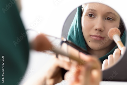 Teenage dirl applying face concealers in front of a mirror. Focus on face