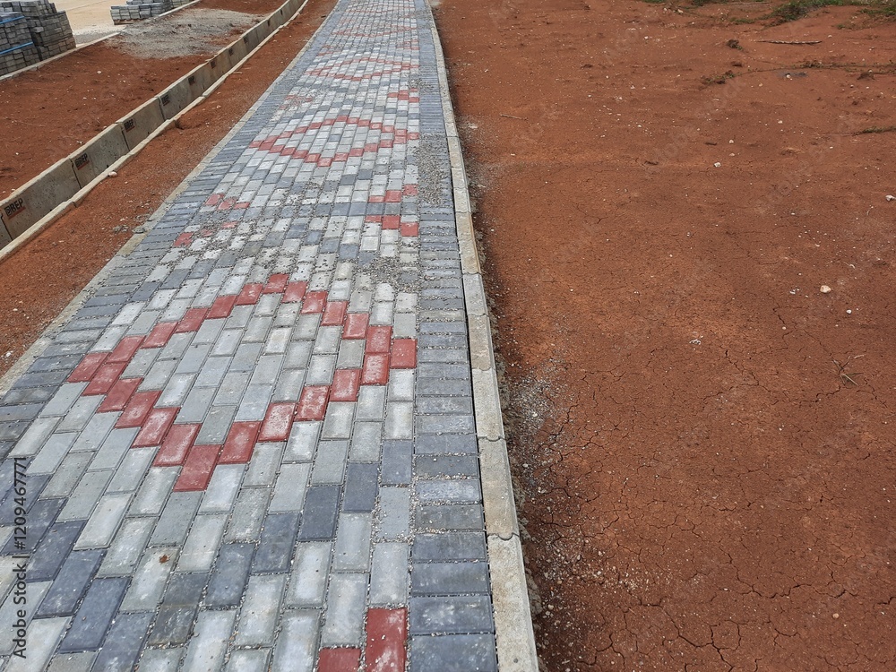 Fototapeta premium Patterned brick walkway surrounded by red soil and unfinished construction work