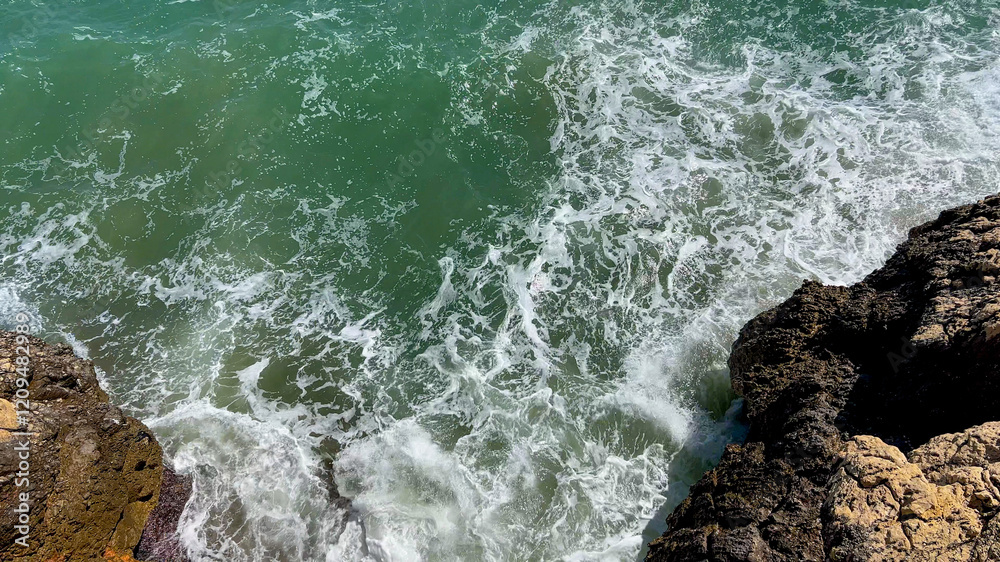 Obraz premium Waves crash against rugged rocks, symbolizing nature's power and serenity, ideal for concepts of tranquility and coastal holidays