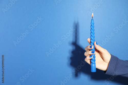 Woman holding burning candle on blue background, closeup. Space for text photo