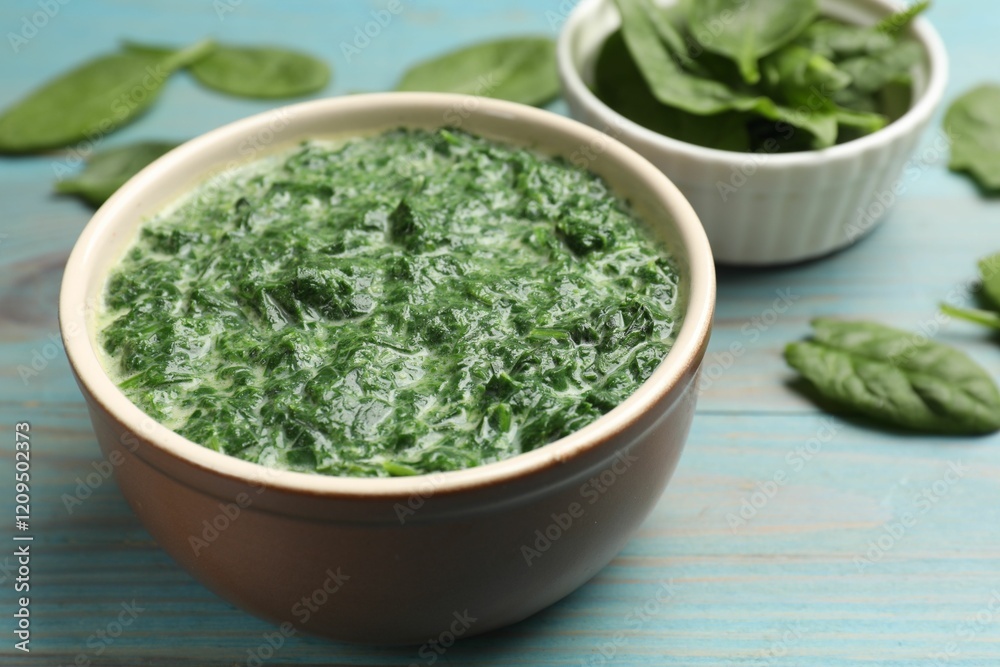 Delicious spinach sauce in bowl and leaves on light blue wooden table, closeup Delicious spinach sauce in bowl and leaves on light blue wooden table, closeup