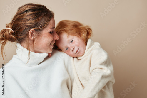 Mother and daughter embracing in cozy sweaters on neutral background for fashion magazine editorial