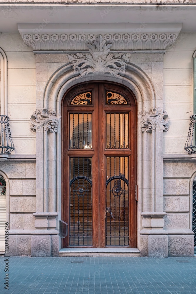 Stunning Art Nouveau entrance featuring a grand wooden door with wrought iron details, framed by expertly carved stone archway with floral motifs. Located in Barcelona's iconic Eixample district
