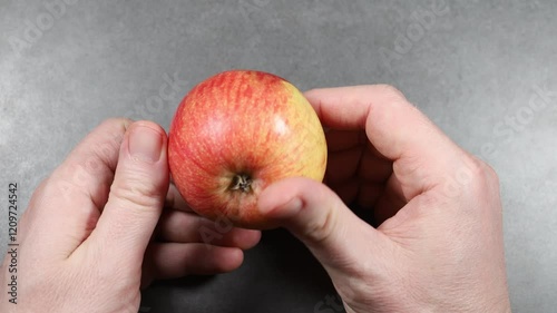 Hands holding a fresh apple on a gray surface