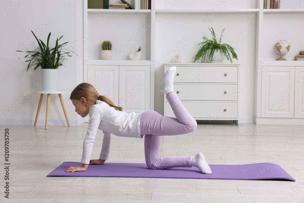 Fototapeta premium Cute little girl exercising on fitness mat indoors