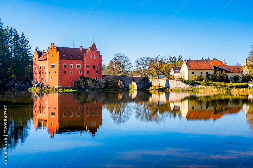 Obraz premium Panoramic view of Cervena Lhota Castle in the Czech Republic, surrounded by a lake reflecting its image. Autumn trees in vibrant colors and sunny weather create a picturesque, serene scene.