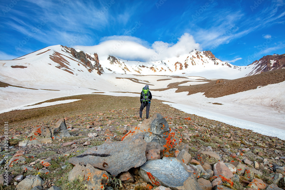 Adventurer explores snowy mountains under a vibrant sky in a remote wilderness