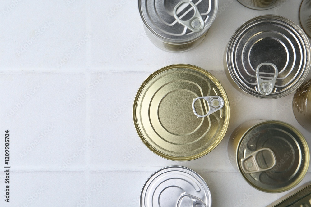 Many closed tin cans on white tiled table, flat lay. Space for text Many closed tin cans on white tiled table, flat lay. Space for text