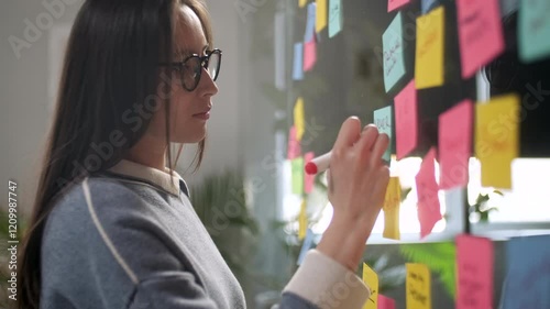Asian Business Woman Write Tasks Creative Ideas On Sticky Notes On Glass Board, Female Corporate Leader Planning Project On Post It Sticky Notes Organize Work On Stickers