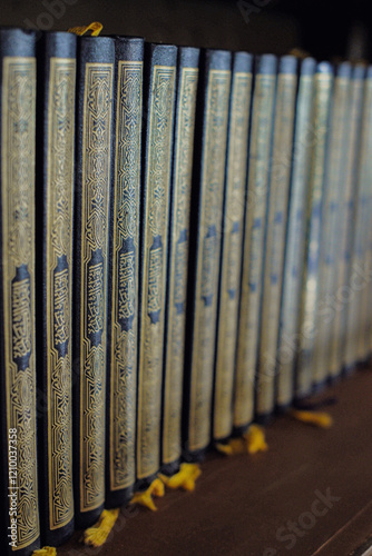 Rows of Qurans on a bookshelf, photographed with focus on one Quran photo