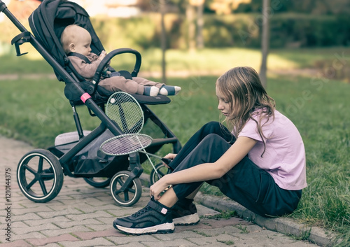 Generagirl and baby in stroller in park, sister with little brother on walk in parkted Image