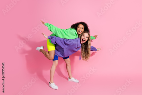 Valokuvatapetti Two cheerful young women in colorful hoodies posing playfully against a vibrant