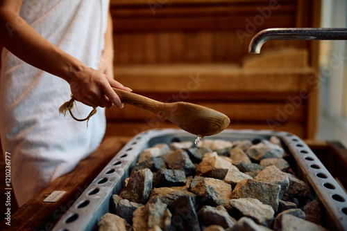 Close up of woman pouring water on hot rocks in sauna.