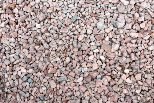 A texture-rich close-up of small, rough gravel stones in shades of pink, gray, and beige. The natural uneven surface and dispersed colors provide an organic appeal. Background for design projects. photo