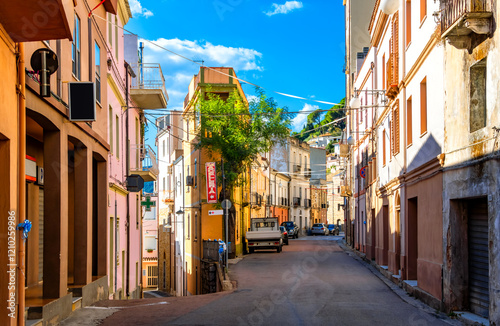 Idyllic, deserted street scene in the picturesque mountain village of Baunei on the Italian Mediterranean island of Sardinia. Main street lined with colorfully painted old houses on a hot summer day. photo